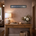 Living room with wooden console table, lamp, and decorative items against a beige wall with a black and silver sign reading ABSOFUCKINGLUTELY.