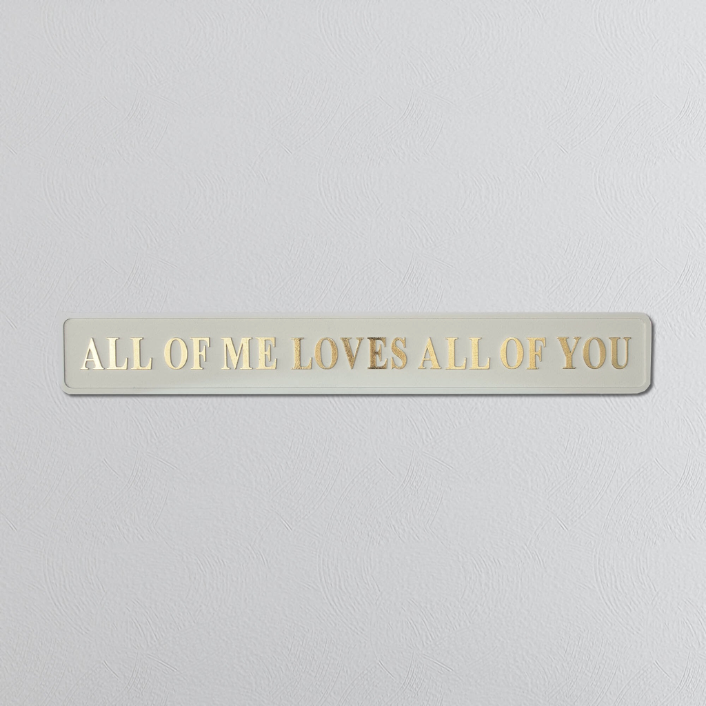 Foil plaque with 'ALL OF ME LOVES ALL OF YOU' text on a light gray background