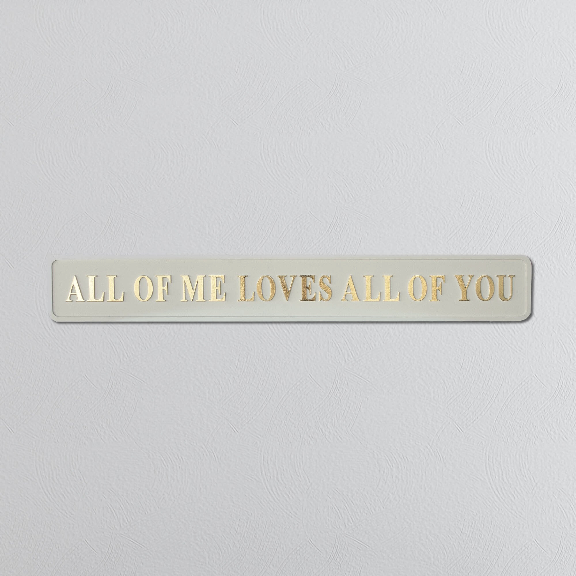 Foil plaque with 'ALL OF ME LOVES ALL OF YOU' text on a light gray background