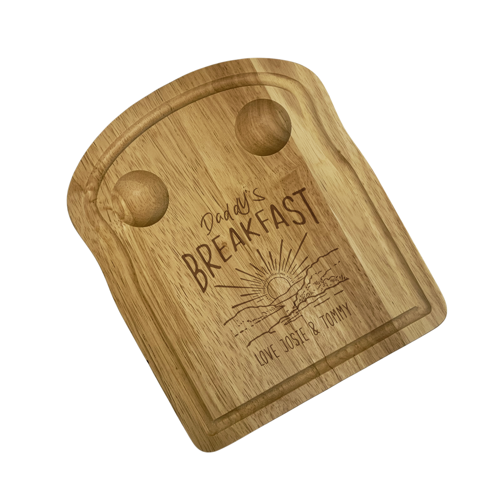 Wooden toast shaped serving board with 2 carved egg holders in the top, an engraved illustration of a sunset with 'Daddy's Breakfast' above it and a personalised message engraved at the bottom.
