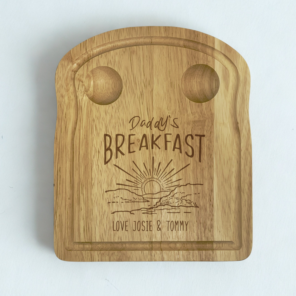 Wooden toast shaped serving board with 2 carved egg holders in the top, an engraved illustration of a sunset with 'Daddy's Breakfast' above it and a personalised message engraved at the bottom.