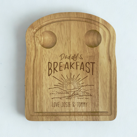 Wooden toast shaped serving board with 2 carved egg holders in the top, an engraved illustration of a sunset with 'Daddy's Breakfast' above it and a personalised message engraved at the bottom.