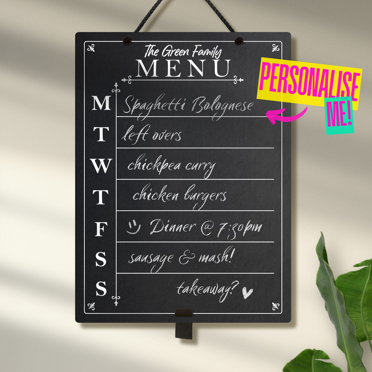 Large chalkboard hanging from black rope with adjustable pen holder at the bottom. Featuring the days of the week printed down the left hand side with sections for each day and the heading 'The Green Family Menu' at the top. A colourful sign reads "Personalise me!" whilst pointing towards the product.
