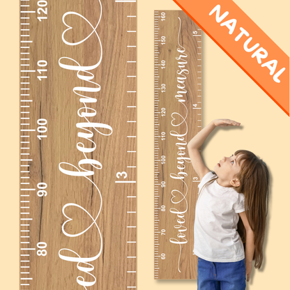 Natural wooden growth chart with measurement scale and 'loved beyond measure' in cursive printed up the middle, and child reaching for it, against a beige background.