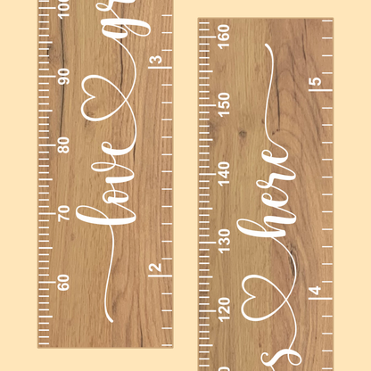 Close up of a wooden growth chart with the words 'love grows here' in cursive script printed up the center in white