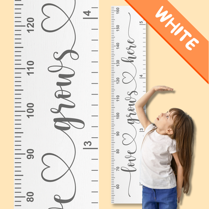 White growth chart with the words 'love grows here' in cursive script printed up the center in grey, with a child measuring their height against it