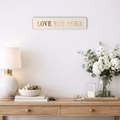 Decorative console table with 'LOVE YOU MORE' sign, lamp, books, and flowers.