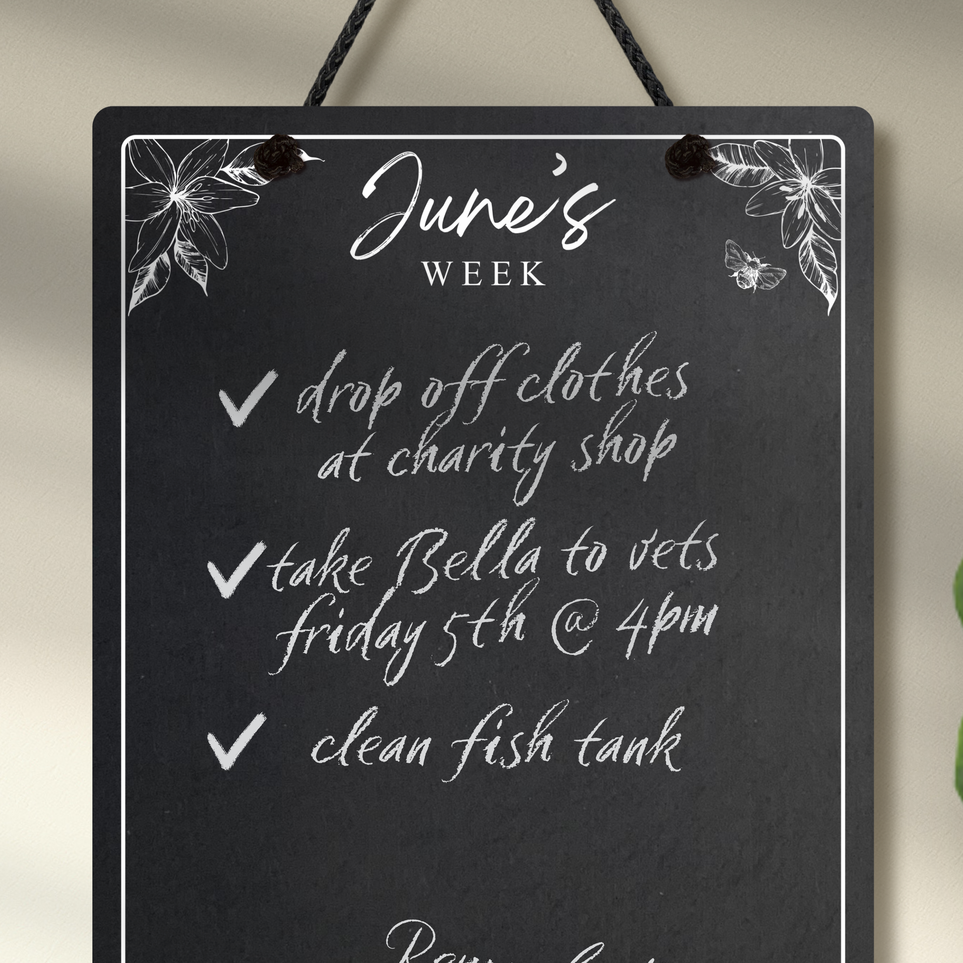 Close up of the medium portrait chalkboard hanging with black rope, featuring sketchy floral illustrations framing a mostly empty space with 'June's Week' at the top in cursive font.