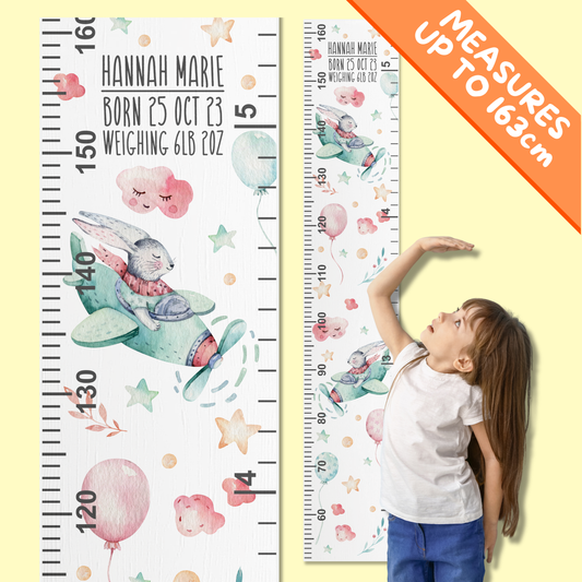 Children's growth charts with watercolour bunnies flying a plane in the clouds. A little girl is demonstrating how to use it by standing in front