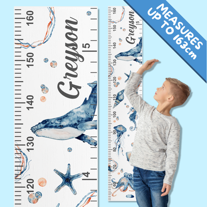 Child standing next to a under the sea themed growth chart with personalised dname printed on it.