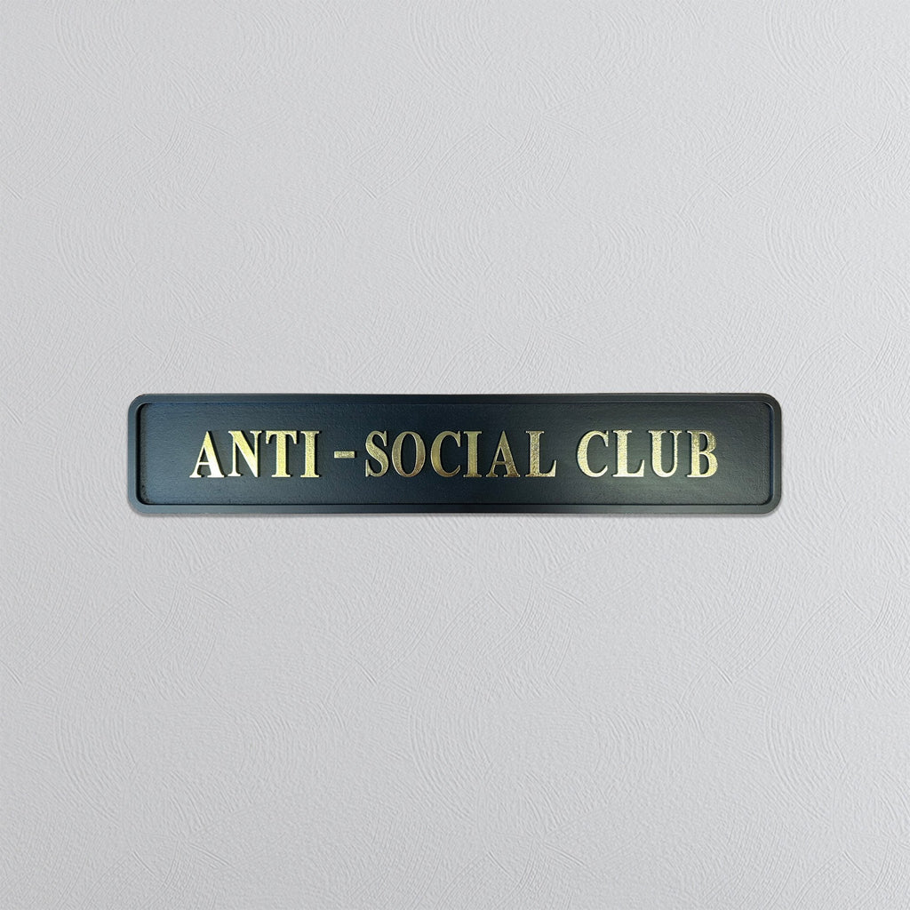 Black street sign with 'ANTI-SOCIAL CLUB' gold text on a light gray background