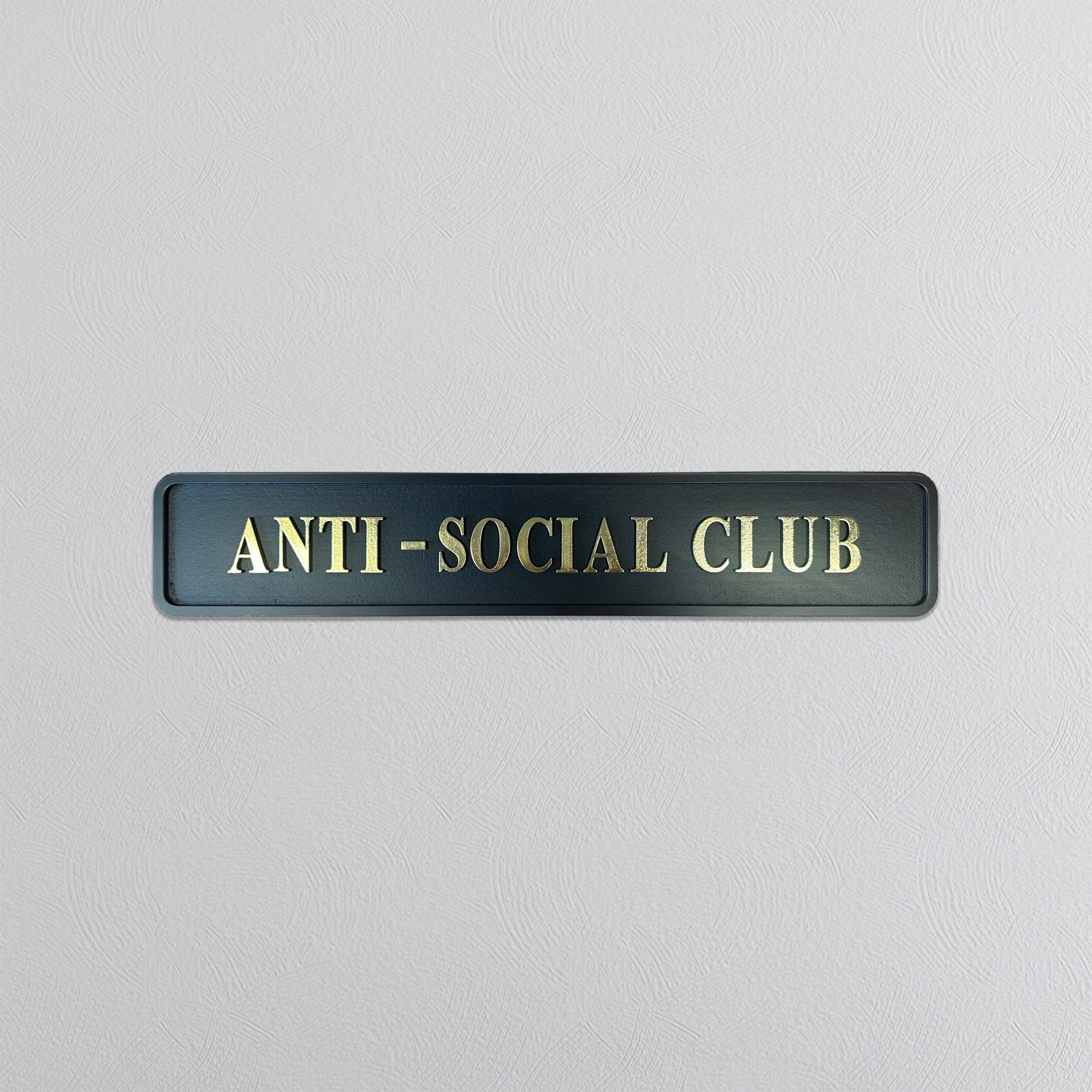 Black street sign with 'ANTI-SOCIAL CLUB' gold text on a light gray background