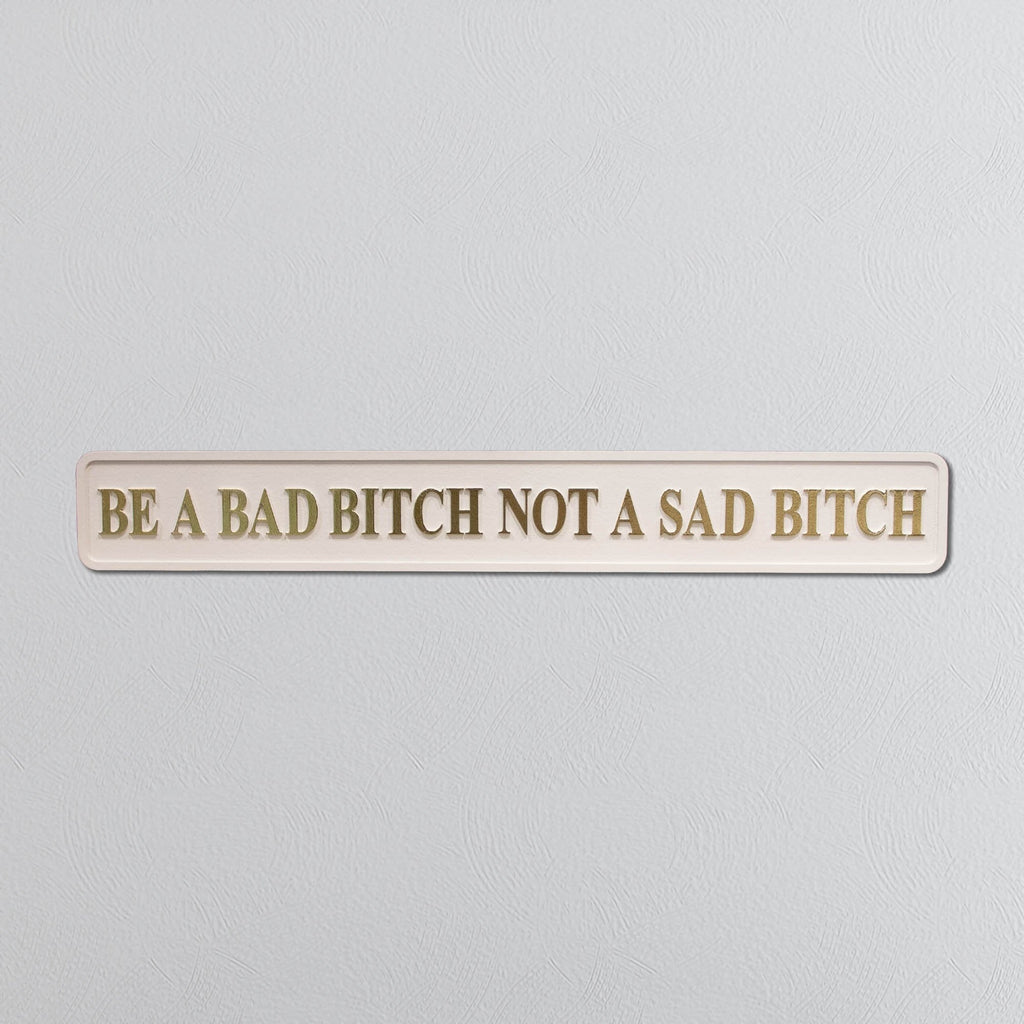 Wooden sign with motivational quote 'Be a bad bitch not a sad bitch' on a light gray background