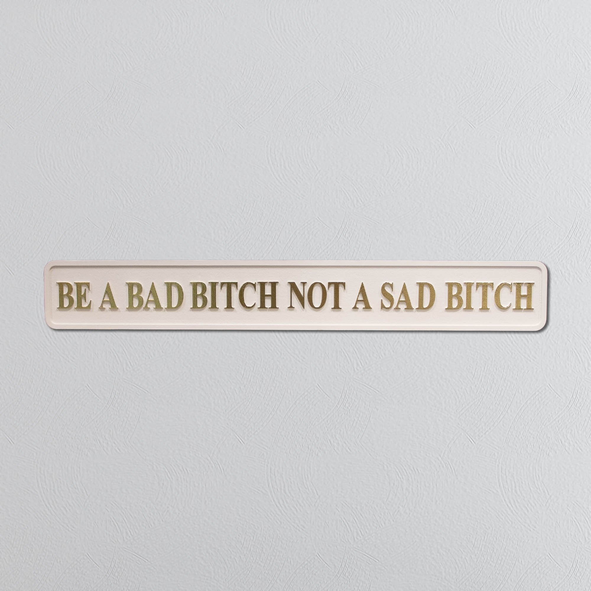 Wooden sign with motivational quote 'Be a bad bitch not a sad bitch' on a light gray background