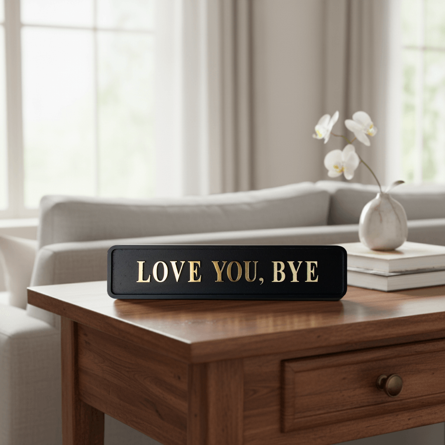 Black and gold foiled street sign with "love you, bye" lettering on a coffee table