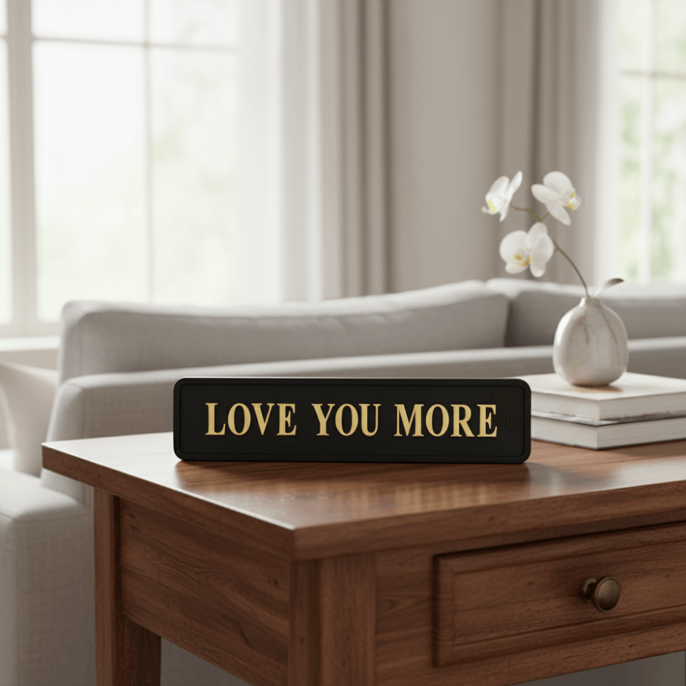 Black with gold foiled street sigh with "love you more" wording on a polished table