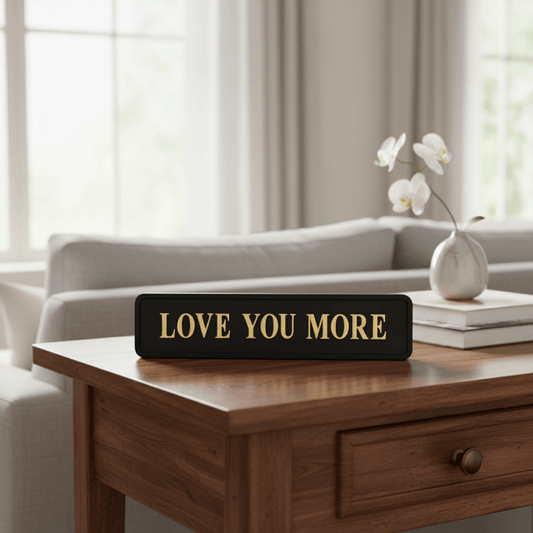 Black with gold foiled street sigh with "love you more" wording on a polished table