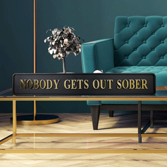 Black and gold foiled street sign with "nobody gets out sober" lettering in a stylish home
