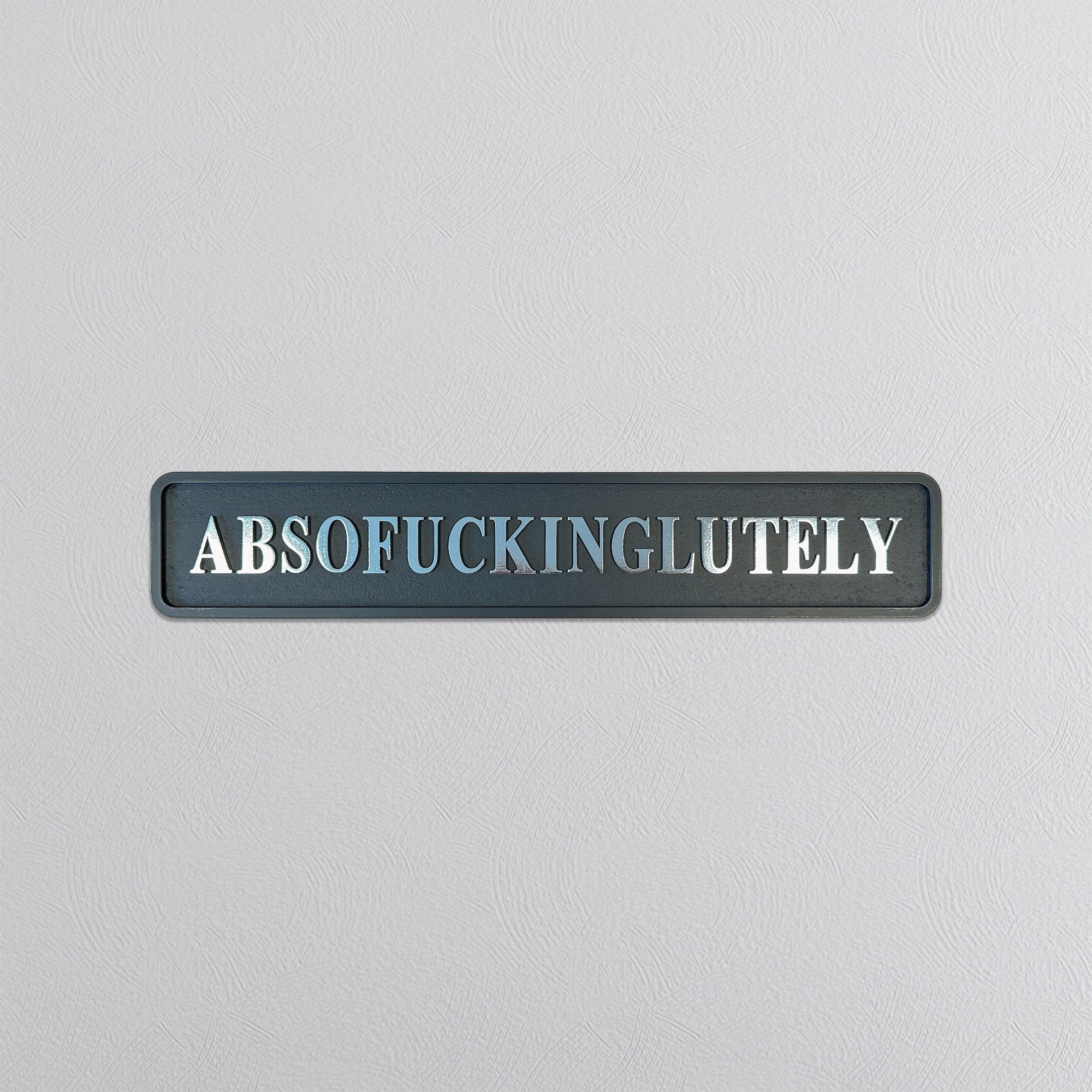 Decorative sign with the word 'ABSOFUCKINGGLUTELY' in silver foil on a gray background