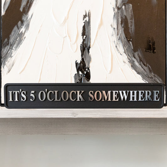 Black and silver foiled street sign with 'It's 5 o'clock somewhere' wording