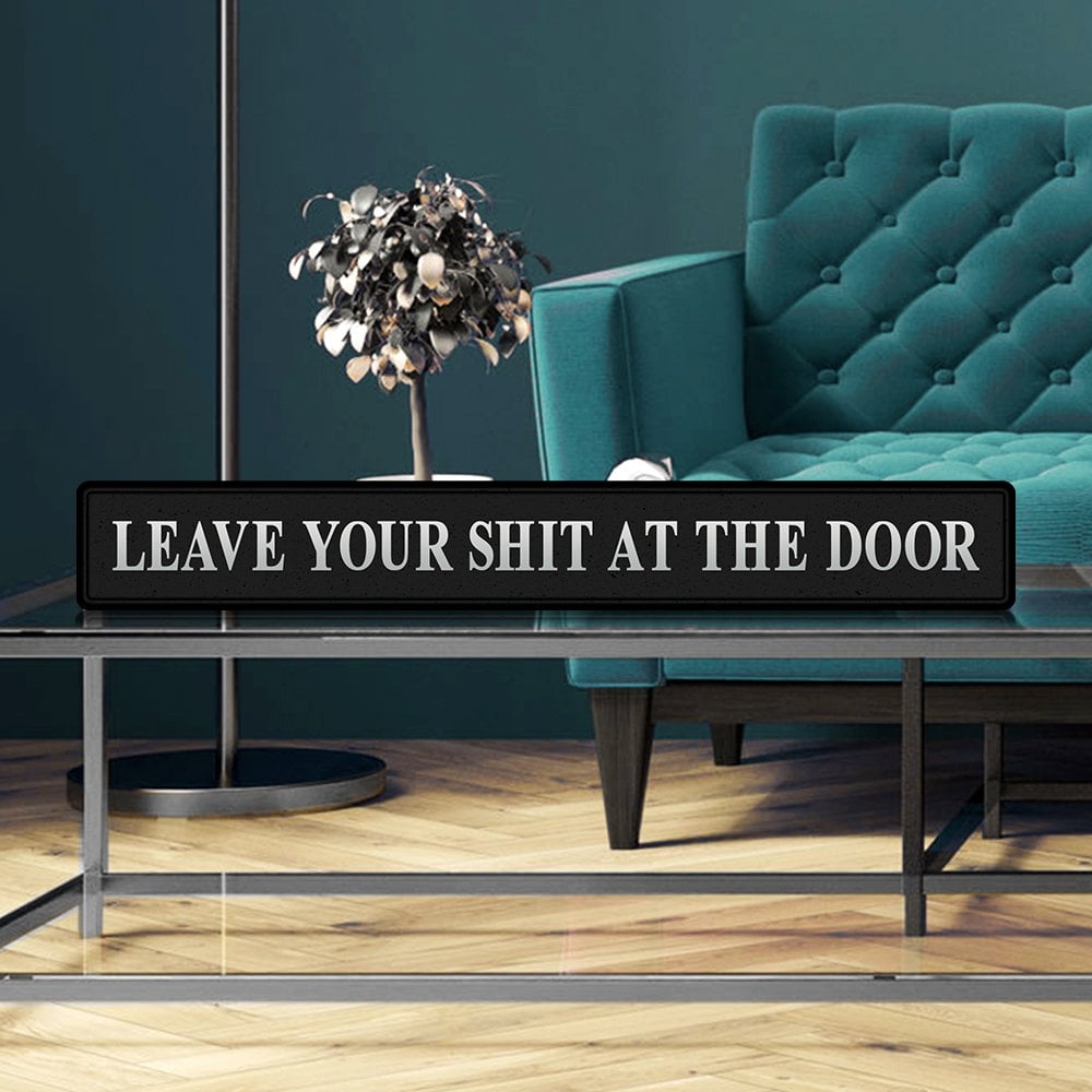 Black decorative sign with LEAVE YOUR SHIT AT THE DOOR in silver text in a stylish living room