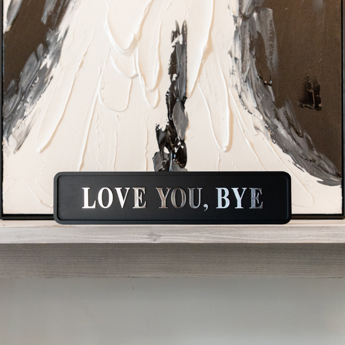 Black and silver foiled street sign with "love you, bye" lettering in front of abstract art