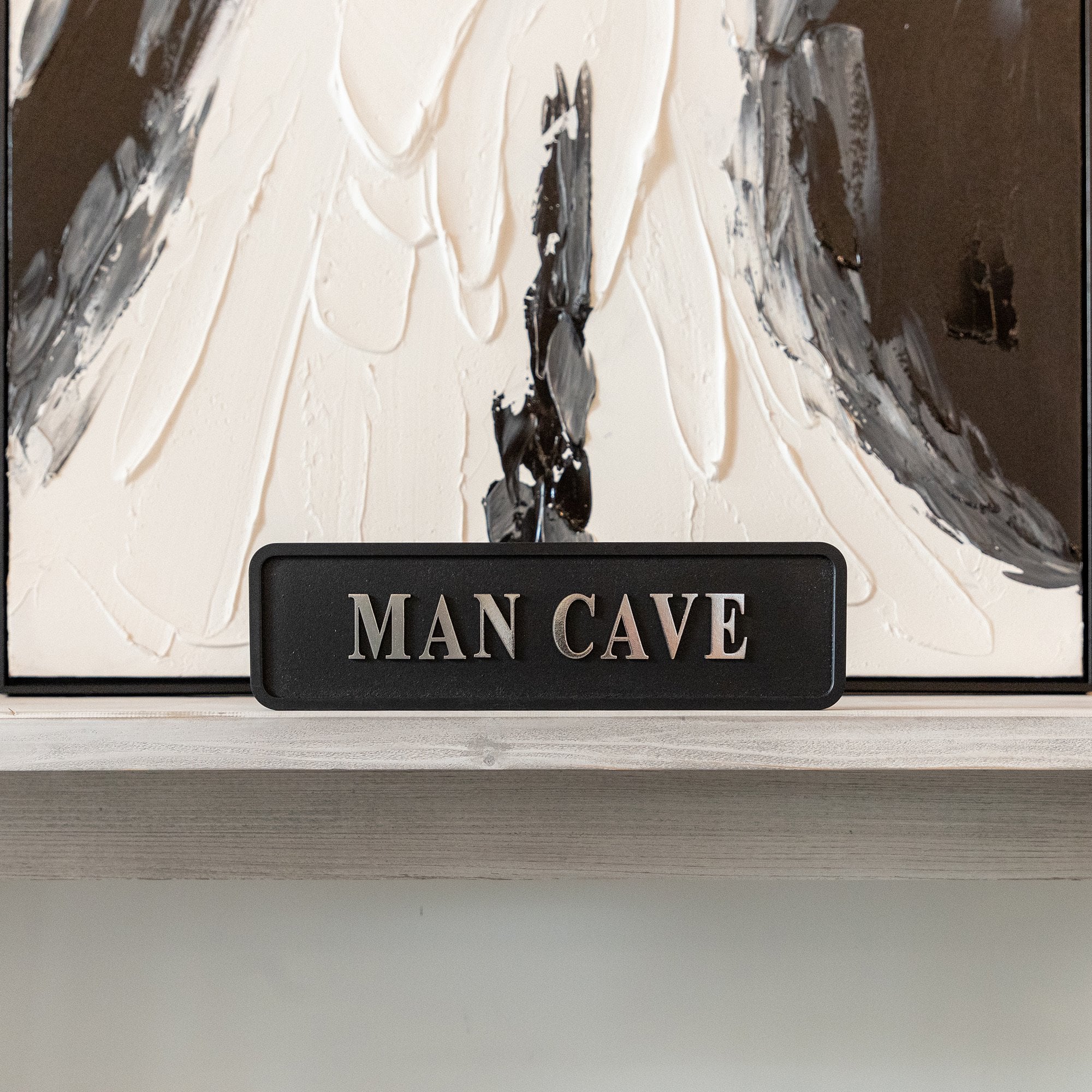 Decorative sign with 'MAN CAVE' silver text in front of abstract art