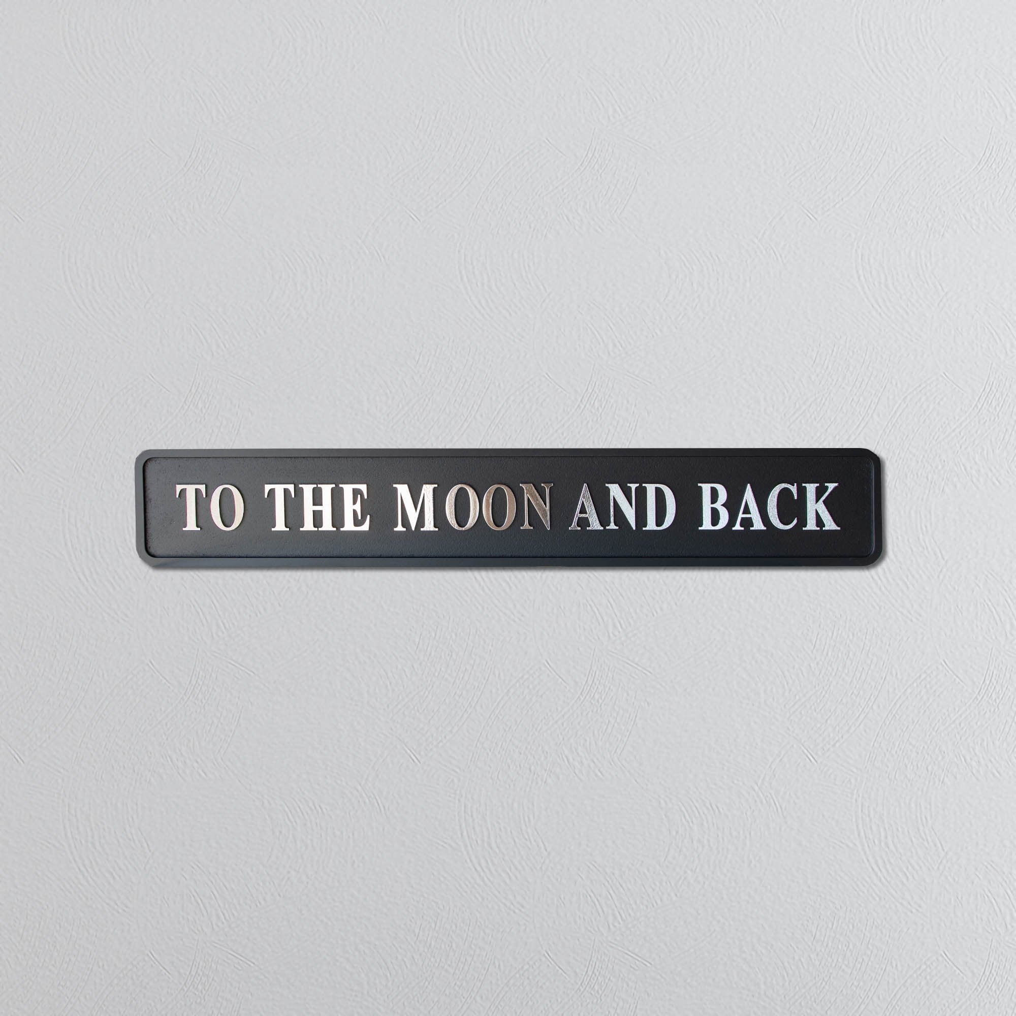 Decorative sign with 'To the Moon and Back' text on a light gray background