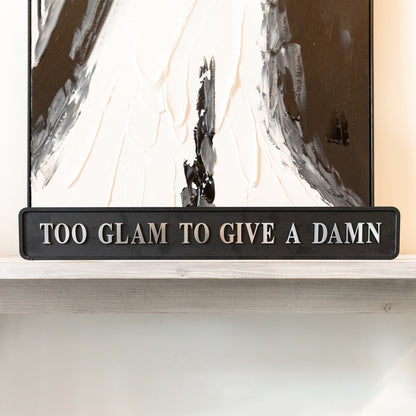 Black and silver foiled street sign with 'Too glam to give a damn' wording