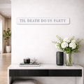 Decorative wall sign with silver text reading TIL DEATH DO US PARTY above a white console table with decorative items.