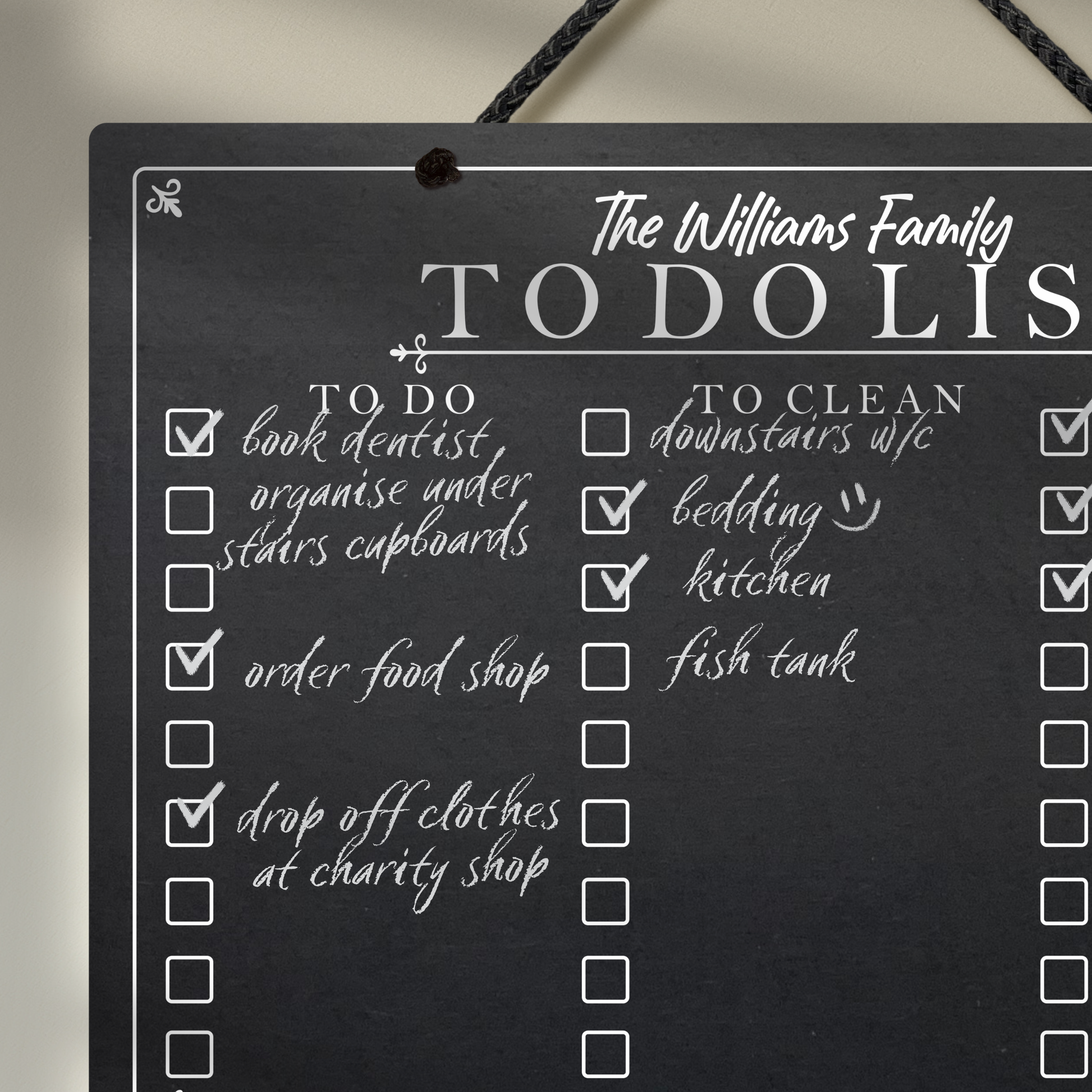 Close up of a chalkboard hanging from black rope featuring printed 'to do' 'to clean' collumn headers with check boxes and 'The Williams Family To Do List' at the top.