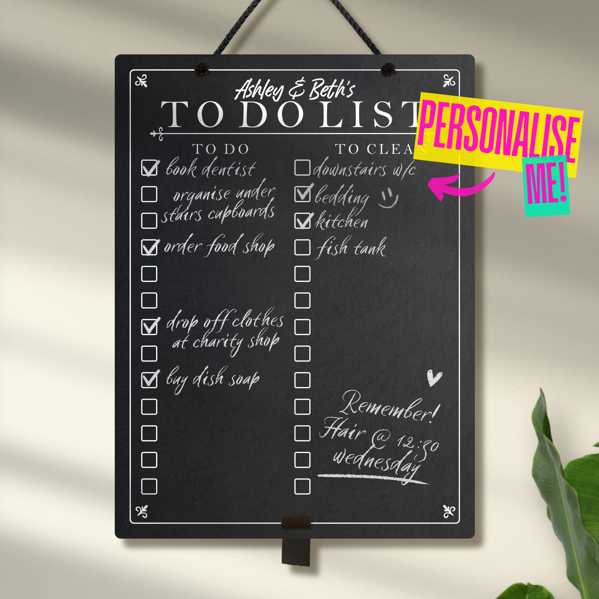 Large portrait chalkboard hanging from black rope with an adjustable elastic pen holder at the bottom. Featuring printed 'to do' and 'to clean' collumn headers with check boxes and 'Ashley & Beth's To Do List' at the top. A colourful sign saying 'Personalise me' points towards the chalkboard.
