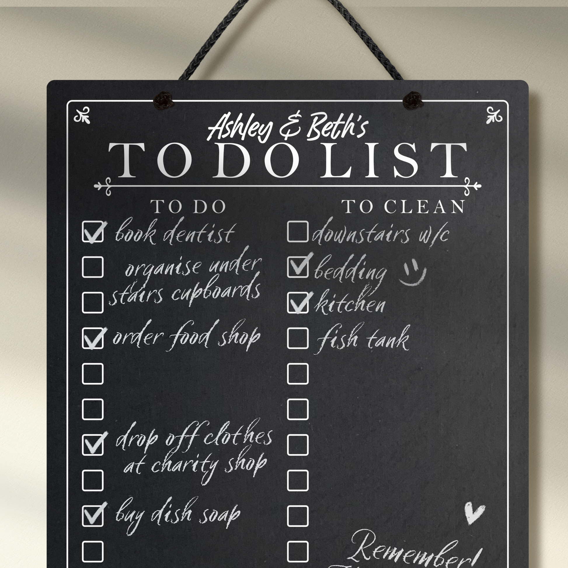 Close up of a chalkboard hanging from black rope featuring printed 'to do' 'to clean' collumn headers with check boxes and 'The Williams Family To Do List' at the top.