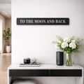 Decorative sign 'To the Moon and Back' above a white console table with a vase of flowers.