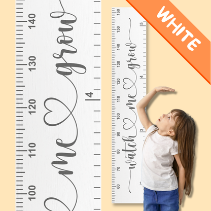 White growth chart with cursive script printed up the middle saying 'watch me grow' in grey, and a child standing next to it against a beige background.