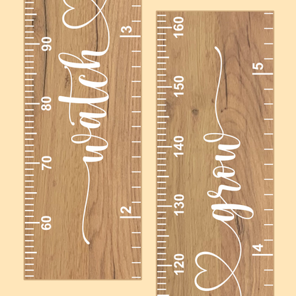 Close up of a wooden growth chart with cursive script printed up the middle saying 'watch me grow' in white